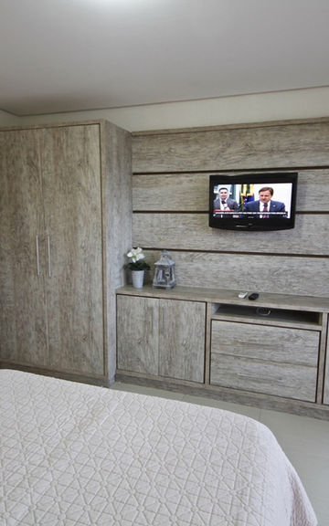 Quarto iluminado com móveis planejados em tons claros e TV fixa no painel.