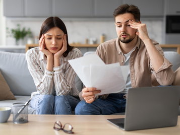 Worried couple reviewing bills and financial paperwork at home.