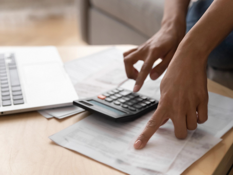 Business owner using a calculator over financial documents beside a laptop.