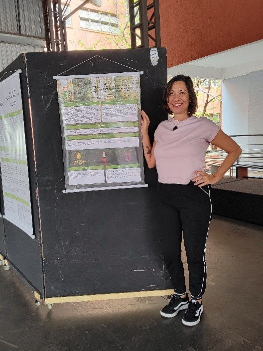 Mulher de aproximadamente 40 anos de calça jogguing preta, camiseta rosa e tenis preto em evento ao lado de banner