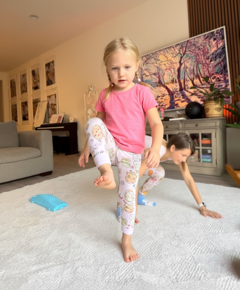 Young child doing a heel raise exercise barefoot on a rug with mom watching nearby