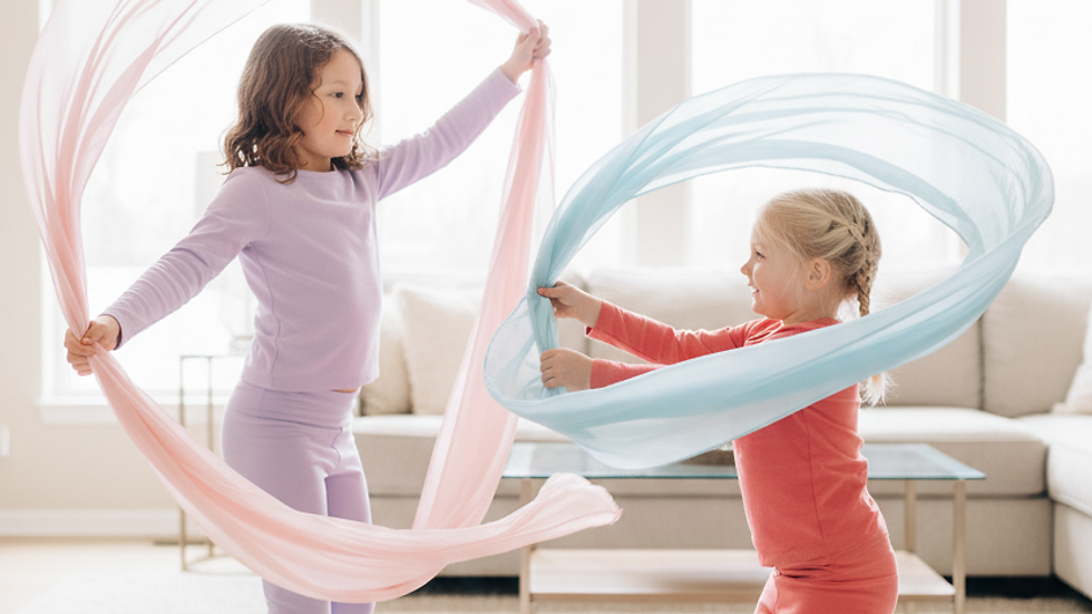 Two kids dancing with scarves in a bright living room barefoot and smiling