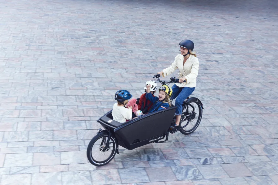 Une maman et 3 enfants circulent sur un vélo cargo biporteur