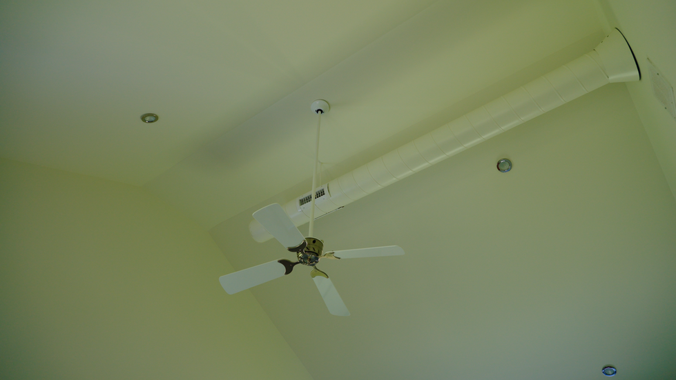 Ceiling-mounted white fan with exposed round duct and recessed lighting in minimalist room