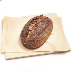 A freshly baked loaf of sourdough bread rests on a piece of parchment paper, ready to be sliced and enjoyed.