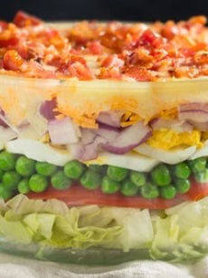 A glass bowl filled to the rim with a delicious layered salad.