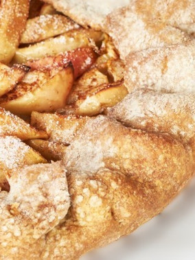 Close-up of a corner of a rustic apple pie with a golden crust and sweet sliced apples dusted with cinnamon and powdered sugar.