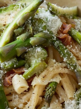 A close-up of pasta, asparagus, and bacon sprinkles with cheese.
