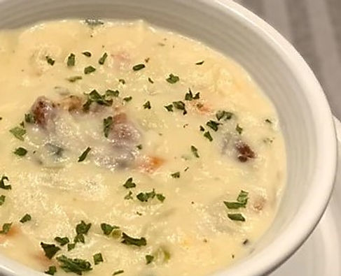 A bowl of creamy potato soup with bits of bacon and sprinkled with parsley. The soup is in a white bowl and sits on a gray dish towel.