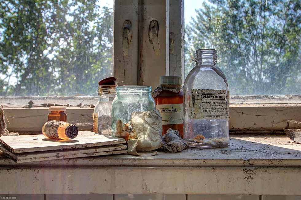 Abandoned medicine bottles and vials gather dust on a sunlit window pane in a Pripyat hospital.