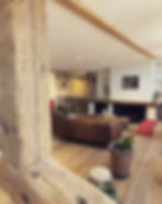 Salon rénové par Unihome Design, poutres en bois ancien apparentes, canapé en cuir cognac, cheminée en pierre et bibliothèque sur mesure en bois clair