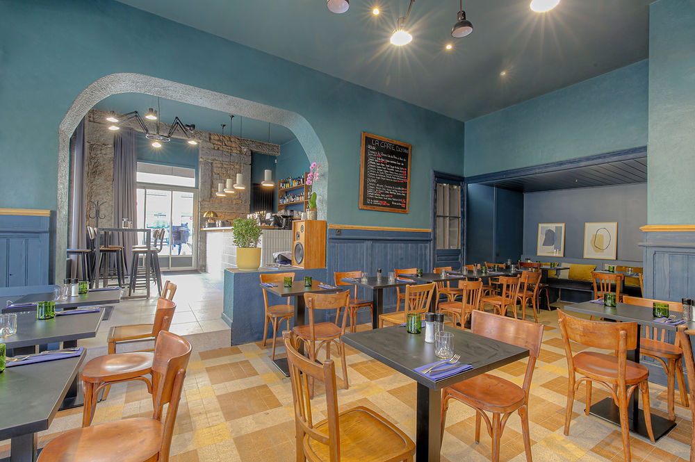 Aménagement intérieur restaurant Lyon par Unihome Design, salle de bar avec comptoir en bois, carrelage blanc en relief, plafond et murs bleu canard, luminaires design et arche en pierre apparente