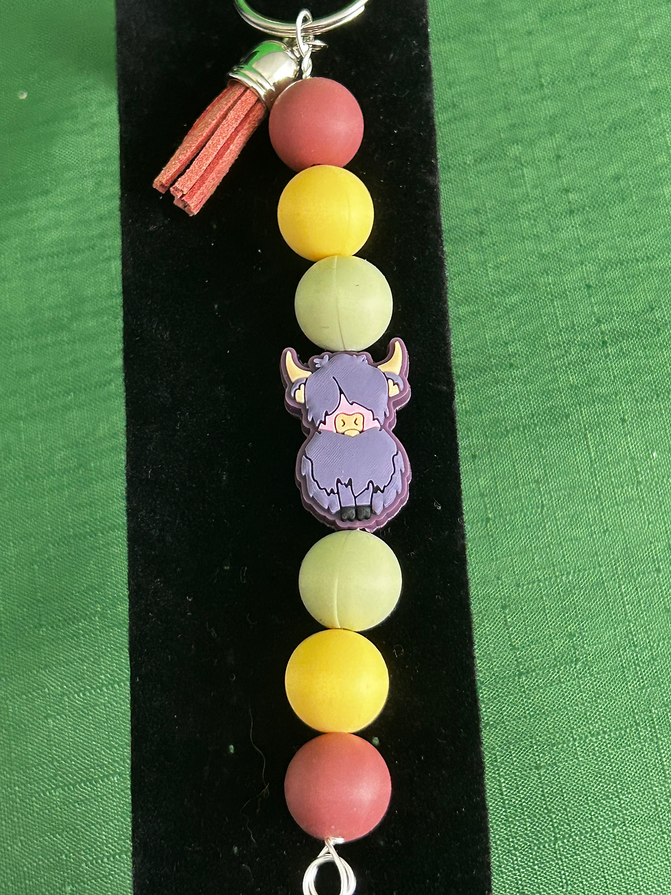 blue/gray highland cow key chain with light green, yellow, and mauve silicone beads