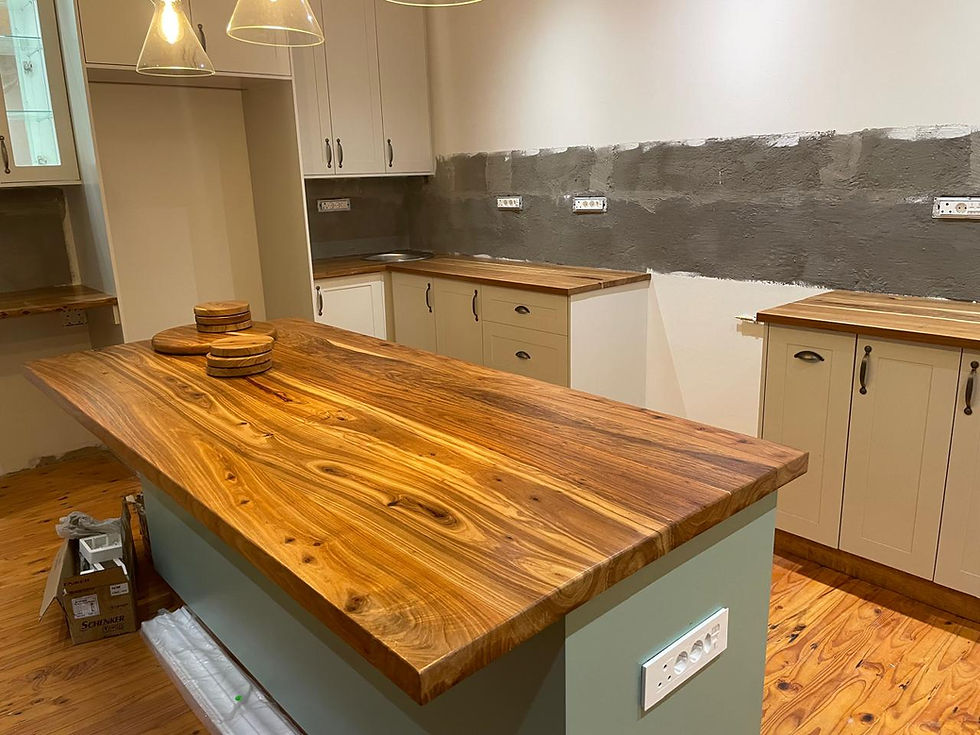 Kiaat Wooden kitchen island in modern kitchen with light cream cabinets, wooden countertops, and pendant lights. Stack of wooden boards on island.