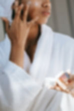 a young woman wearing a white robe and towel on her head is putting on facial cream