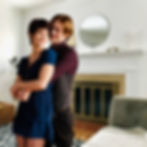 Alice and Jasper standing in the living room and smiling