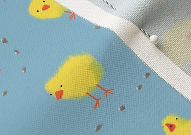 A slightly creased piece of fabric featuring fluffy yellow chicks on a light blue ground pecking at scattered corn by lenes_linien.