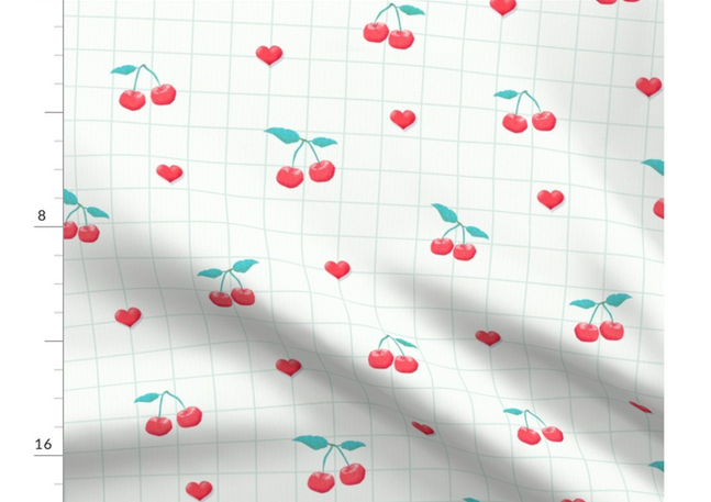 A slightly creased piece of fabric featuring a design of red cherries with green stems, little hearts and a green grid on white by lenes_linien