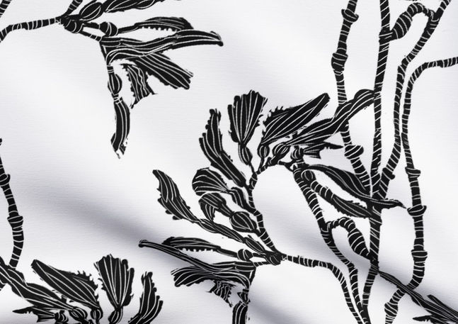 A slightly creased piece of fabric featuring an elegant duotone design of sea kelp fronds in a blockprint style.
