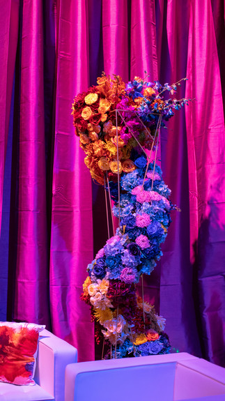 Sculptural vertical floral installation using multicolored roses and hydrangeas against a deep magenta draped backdrop.