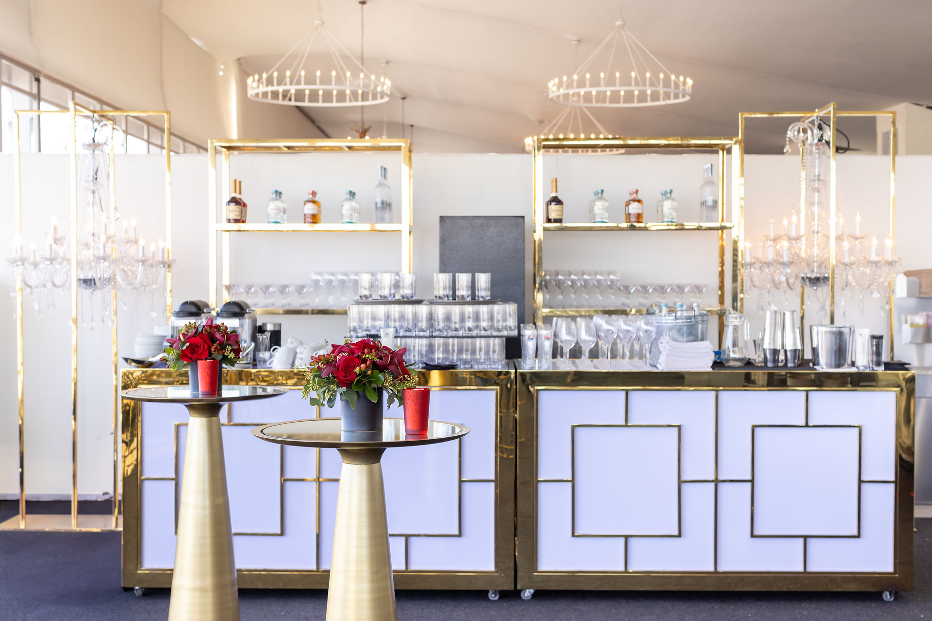 Upscale bar setup with white and gold shelving and red flower accents.