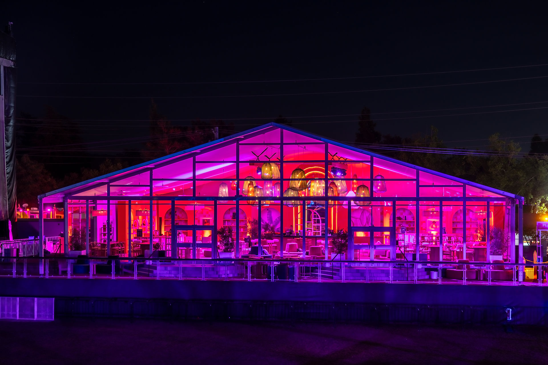 Fuchsia-lit glass tent structure at an outdoor event designed by a full-service event design team