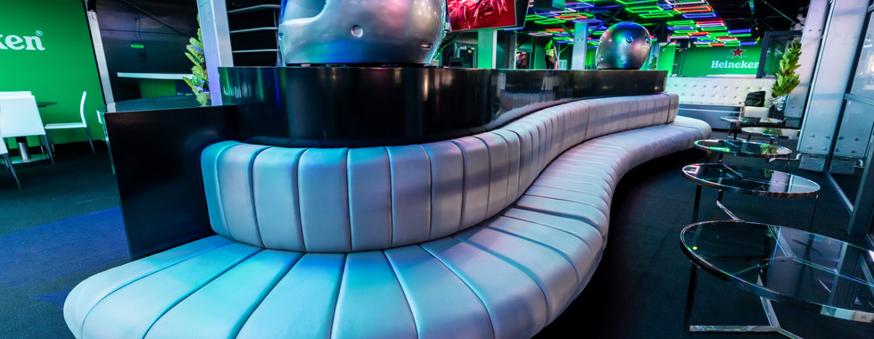 Heineken-branded lounge with neon ceiling lights, curved metallic sofa, and F1 helmet decor