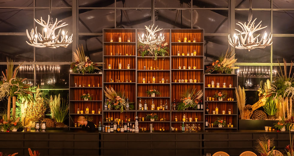 Tented outdoor event bar with warm lighting, floral decor, candles, and antler