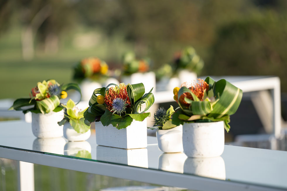 Minimalist tropical floral arrangements in modern white ceramic vases displayed on mirrored outdoor tables.
