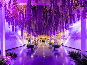 Immersive hallway installation featuring a ceiling canopy of cascading purple and white flowers with uplighting.