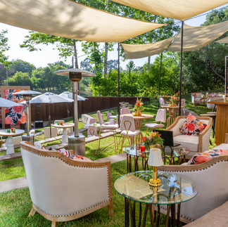 Outdoor lounge setup with white sofas, floral pillows, and canopy panels at a luxury event.