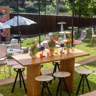 Outdoor wood high-top tables with floral centerpieces and shaded cocktail seating.