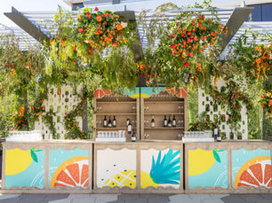 Outdoor bar with greenery, citrus decor, and tropical-themed panels at a summer party setup