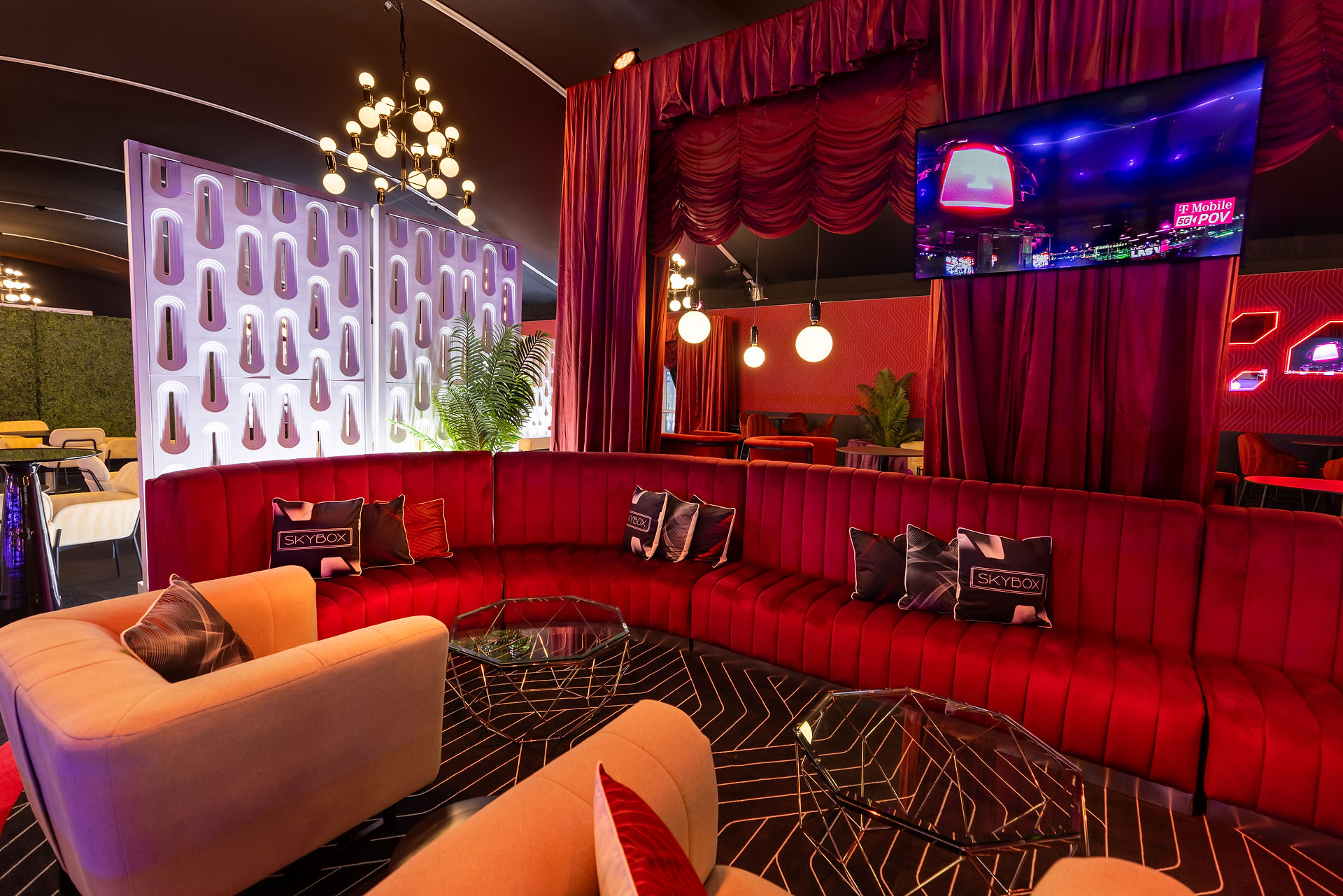 Lounge area with red velvet couches, stage drapery, and mid-century modern lighting at Skybox.