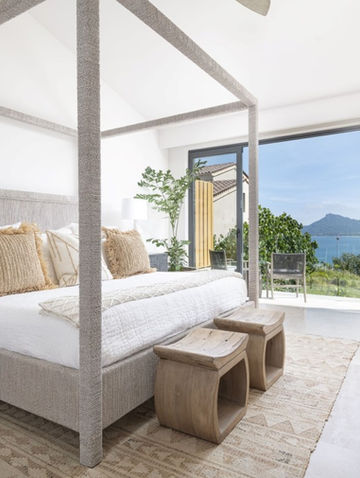 Luxury Vacation Home Serene Master Bedroom with Natural Woven Textures, Wood Furniture Accents, White Walls and a View of the Ocean off the Balcony
