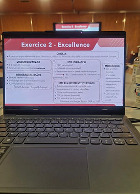 Laptop displaying a Horizon Europe training slide titled “Exercise 2 – Excellence” during a workshop session, with presentation screen visible in the background