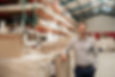Portrait of a smiling warehouse manager leaning against some stock with piles of carpets s