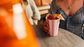 A woman holding a cocktail in a pink and white stripped paper cup with an umberella in it.