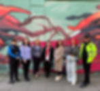 seven women that work in Southend stand in a line in front of a wall with green and red artwork