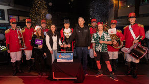A group of people stage on stage in front of a plunger with lights and trees behind them.