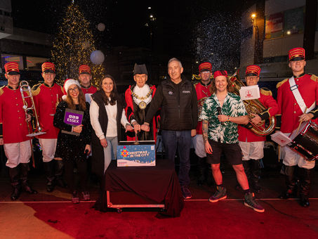 A group of people stage on stage in front of a plunger with lights and trees behind them.