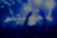 Picture of a person at a concert raising their arms on the air in celebration with stage lights in the background