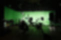 A green screen production studio with lights, microphone, camera and directors chairs.