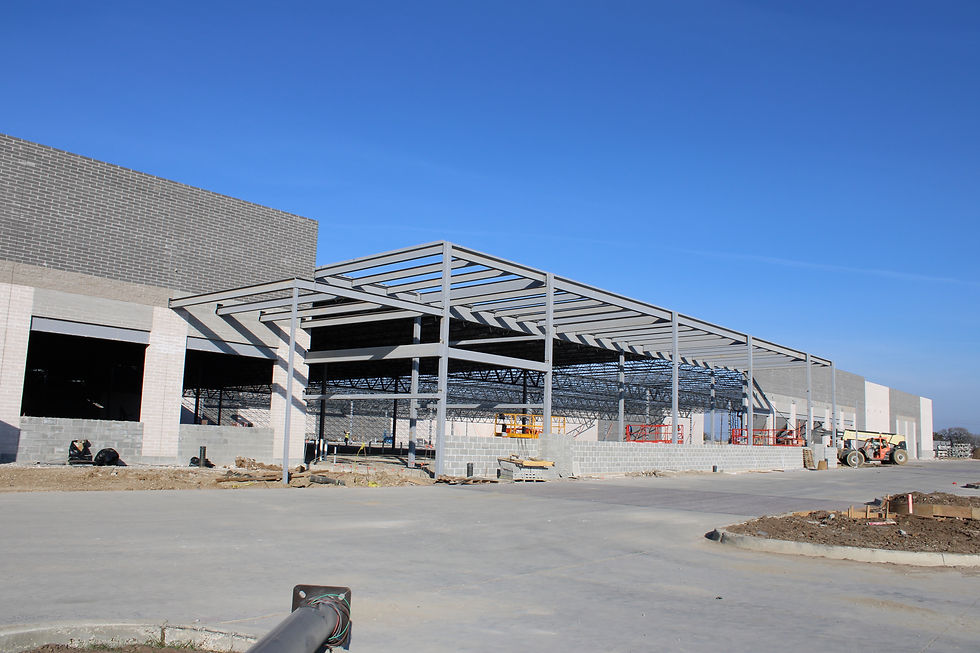 Large warehouse under construction with steel frame, cinderblock walls, a forklift, and a clear blue sky above.