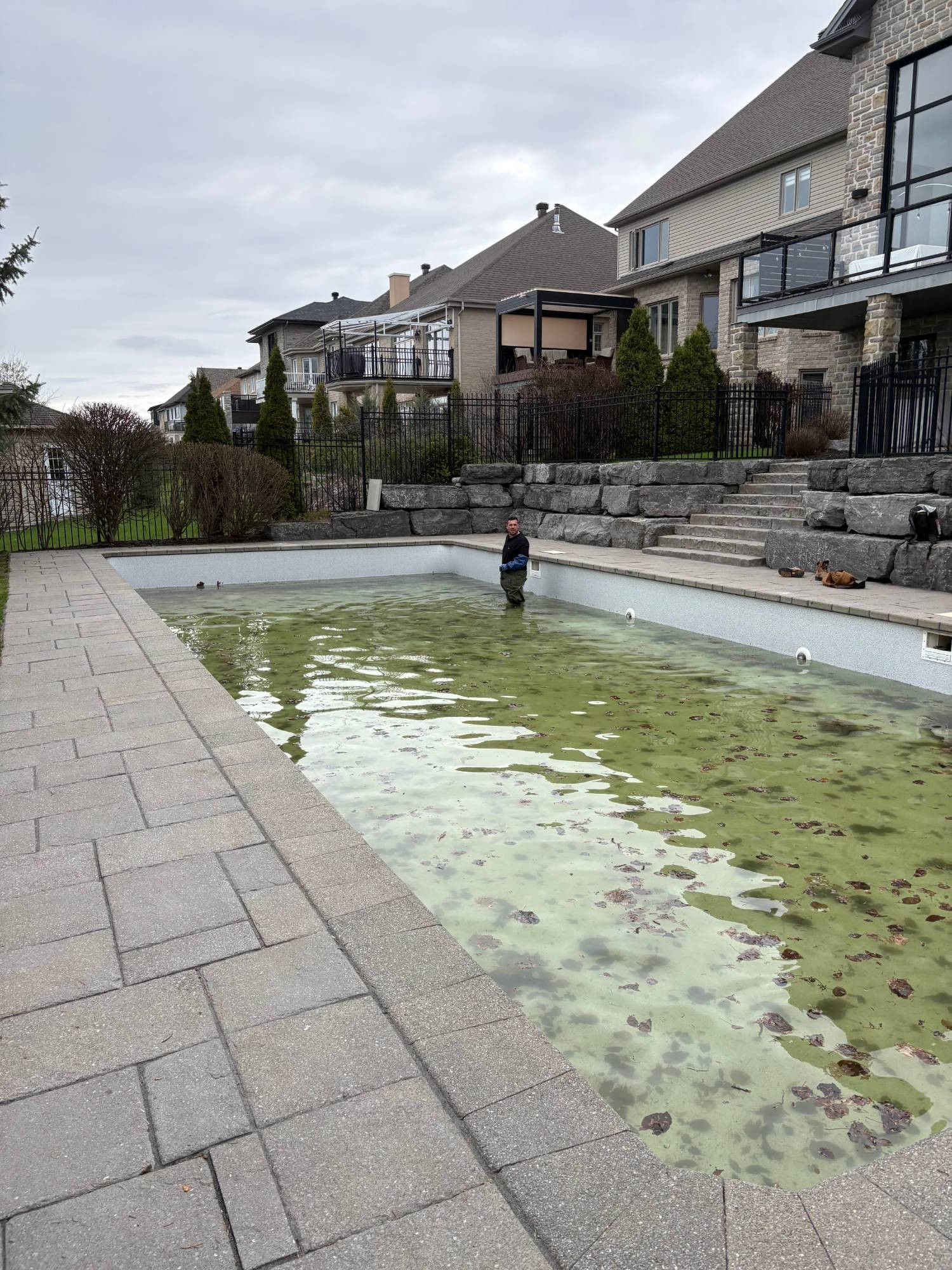 Avant : piscine creusée à l'eau verte, entourée d'un aménagement de pierre