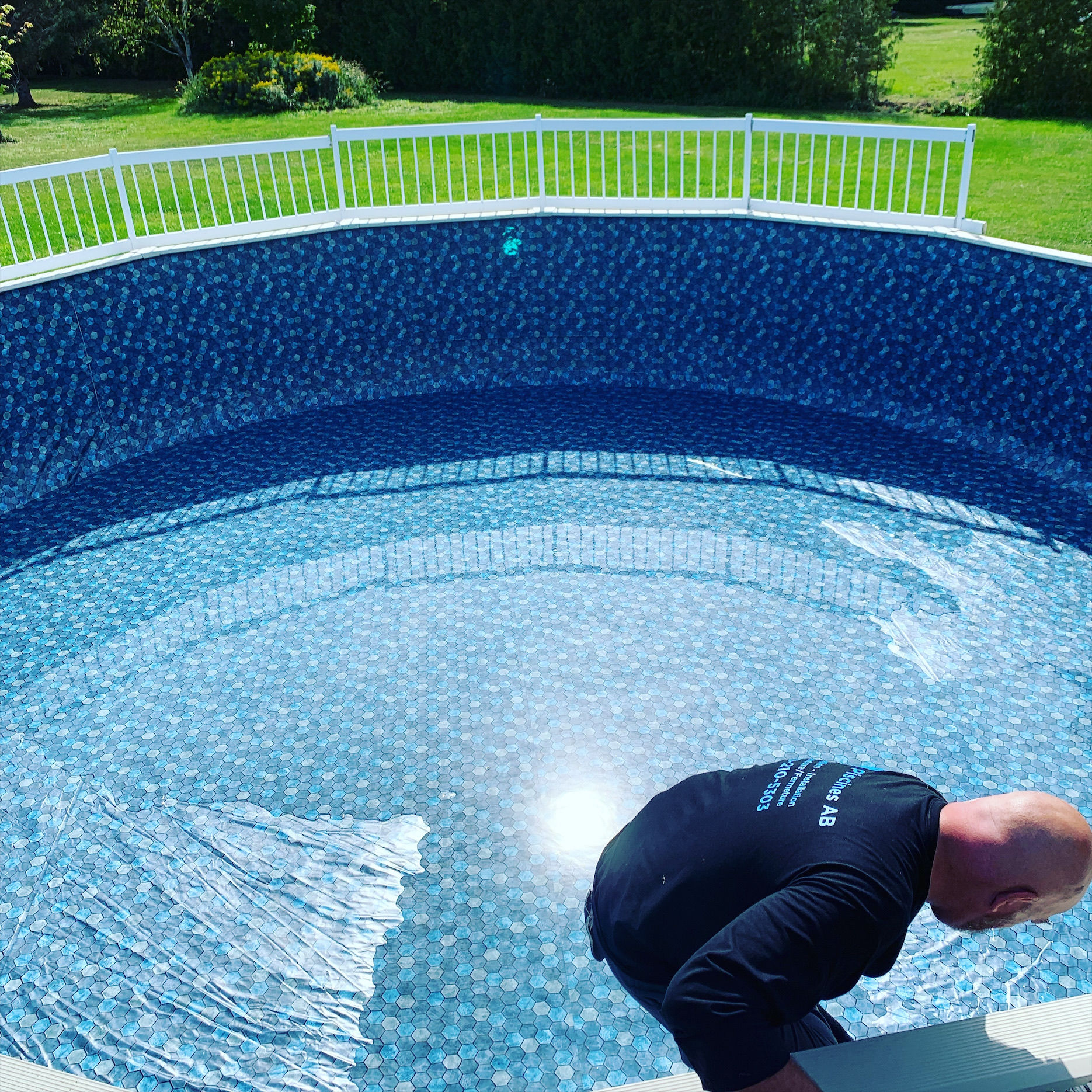 Technicien de Piscines AB, en chandail de l'entreprise, qui installe une toile à motif mosaïque dans une piscine hors terre