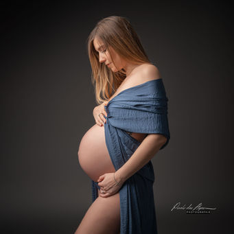Extrait d'une séance grossesse réalisé en studio. La future maman porte un voilage de soie bleu laissant apparaitre son ventre. La personne est de profil