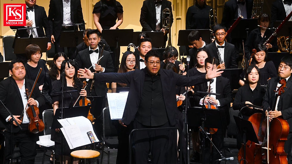 《有誰共鳴》管弦音樂會指揮家郭子健與樂團成員同台謝幕。畫面中央為指揮郭子健張開雙臂致意,後方為完整編制的管弦樂團,包含小提琴、大提琴與管樂手等,場面宏大。