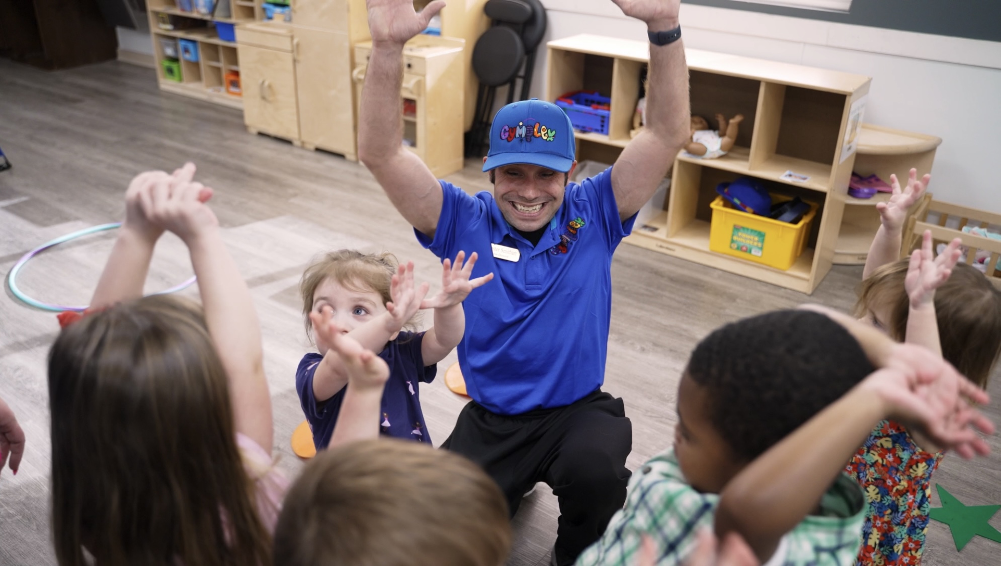A Gymplex coach and preschool children raising their hands together during class