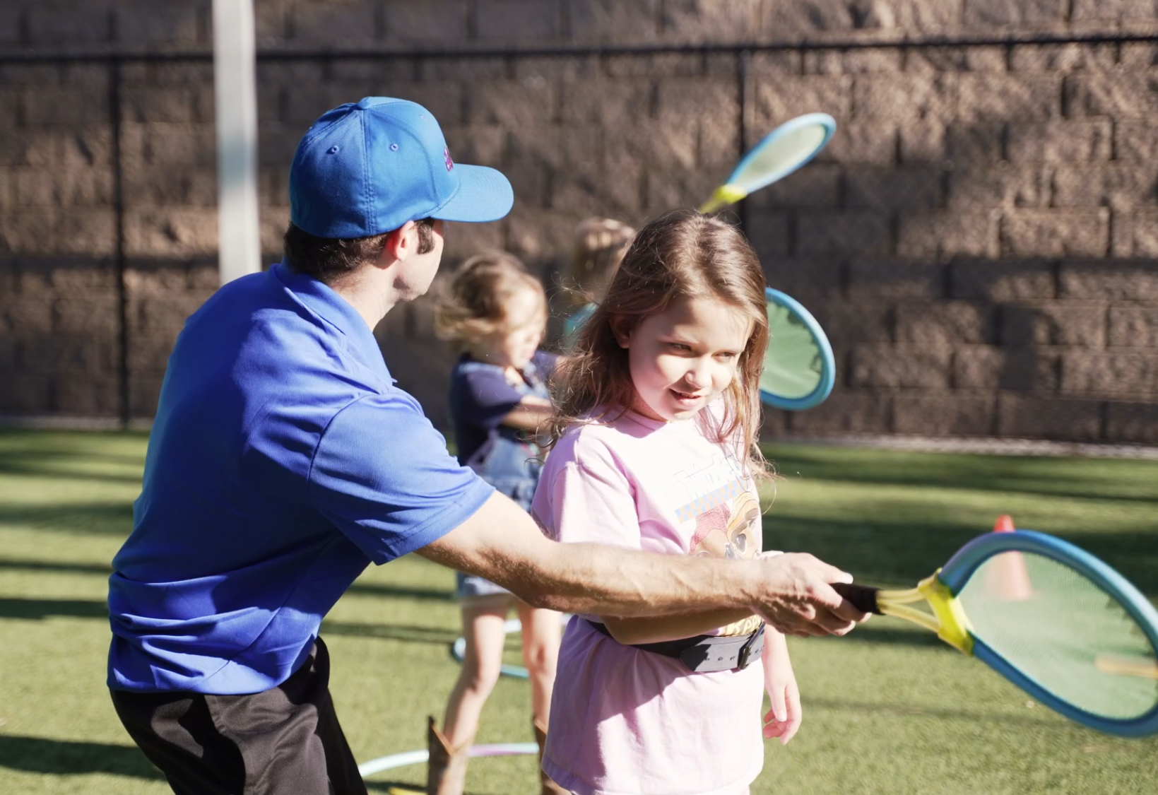 A Gymplex coach helping a child practice a tennis swing